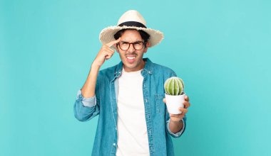 Genç İspanyol adam şaşkın ve şaşkın hissediyor, deli olduğunu ve elinde bir kaktüs tuttuğunu gösteriyor.