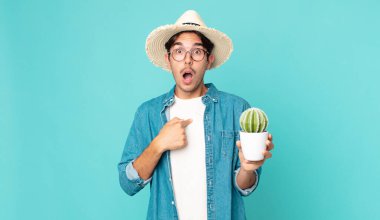 Genç İspanyol adam şok olmuş ve şaşırmış görünüyor ağzı sonuna kadar açık, kendini işaret ediyor ve bir kaktüs tutuyor.