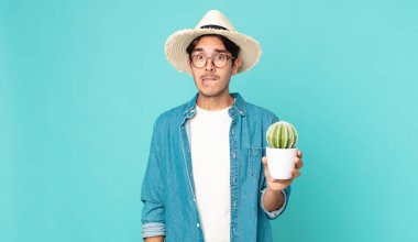 Kafası karışmış ve elinde kaktüs tutan genç İspanyol bir adam.