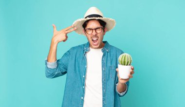 Genç İspanyol adam mutsuz ve stresli görünüyor, intihar jesti silah işareti yapıyor ve elinde kaktüs tutuyor.