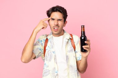 Genç İspanyol adam şaşkın ve şaşkın hissediyor, deli olduğunu ve elinde bir şişe bira tuttuğunu gösteriyor.