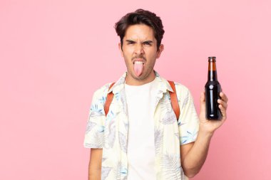 Genç İspanyol bir adam midesi bulanmış ve rahatsız olmuş hissediyor. Dilini dışarı çıkarıyor ve elinde bir şişe bira tutuyor.