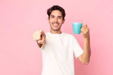 Genç İspanyol bir adam kamerayı işaret ederek seni seçiyor ve elinde kahve fincanı tutuyor.
