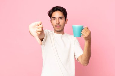 Genç İspanyol bir adam kızgın hissediyor, baş parmağını kaldırıyor ve elinde kahve fincanı tutuyor.