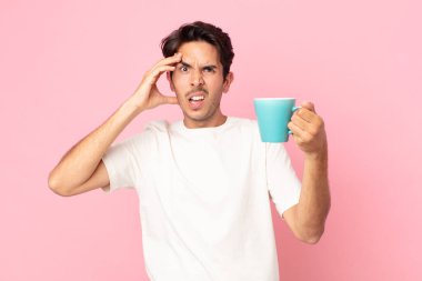 Genç İspanyol adam mutlu, şaşkın ve şaşırmış görünüyor ve elinde bir kahve fincanı tutuyor.