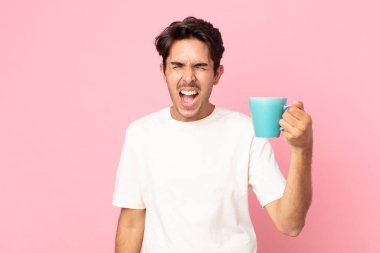 Genç İspanyol adam saldırganca bağırıyor, çok kızgın görünüyor ve elinde kahve fincanı var.