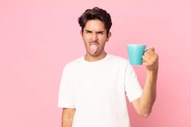 Genç İspanyol bir adam midesi bulanmış ve rahatsız olmuş hissediyor. Dilini dışarı çıkarıyor ve elinde bir kahve fincanı tutuyor.