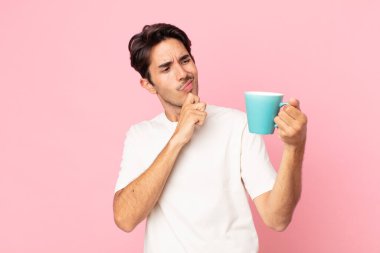 Genç İspanyol bir adam düşünüyor, kuşkulu ve kafası karışık hissediyor ve elinde kahve fincanı tutuyor.