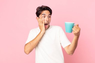 Genç İspanyol adam mutlu, heyecanlı ve şaşırmış hissediyor ve elinde kahve fincanı tutuyor.