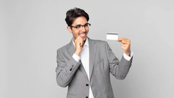 若いヒスパニック系の男は あごに手で幸せと自信を持って表情で笑顔とクレジットカードを保持します — ストック写真