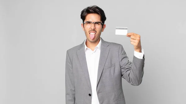 他的惊慌失措的年轻人感到厌恶 吐出舌头 手里拿着一张信用卡 — 图库照片