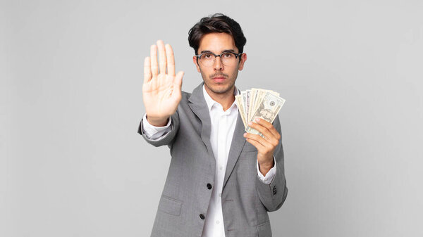 young hispanic man looking serious showing open palm making stop gesture