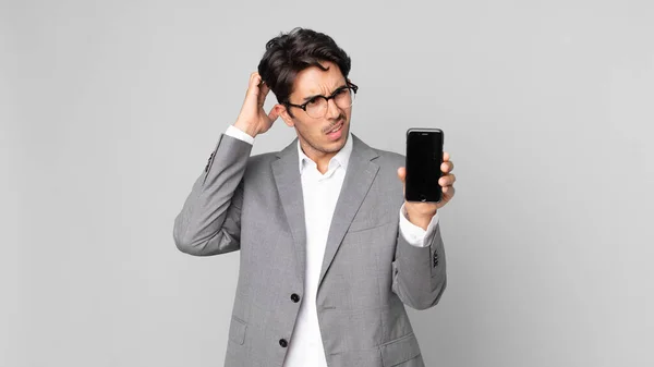 Young Hispanic Man Feeling Puzzled Confused Scratching Head Holding Smartphone — Stock Photo, Image