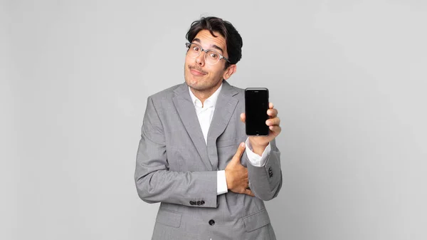 Jovem Hispânico Homem Encolhendo Ombros Sentindo Confuso Incerto Segurando Smartphone — Fotografia de Stock