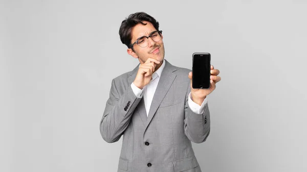 Young Hispanic Man Thinking Feeling Doubtful Confused Holding Smartphone — Stock Photo, Image