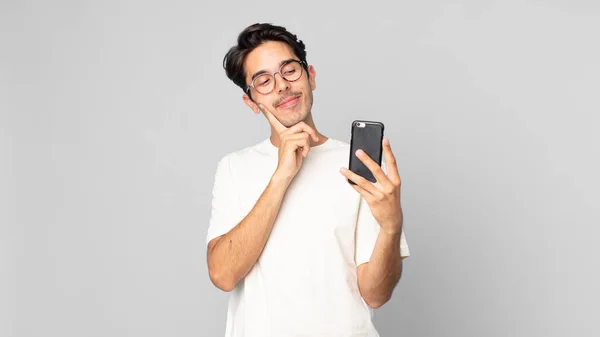Joven Hispano Sonriendo Feliz Soñando Despierto Dudando Sosteniendo Smartphone — Foto de Stock