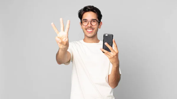 Nuori Latinomies Hymyilee Näyttää Ystävälliseltä Näyttää Numero Kolme Pitää Älypuhelinta — kuvapankkivalokuva