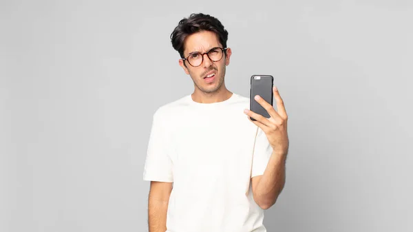 Jovem Hispânico Homem Sentindo Intrigado Confuso Segurando Smartphone — Fotografia de Stock