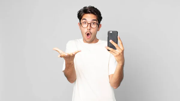 Joven Hispano Sintiéndose Extremadamente Sorprendido Sorprendido Sosteniendo Smartphone —  Fotos de Stock