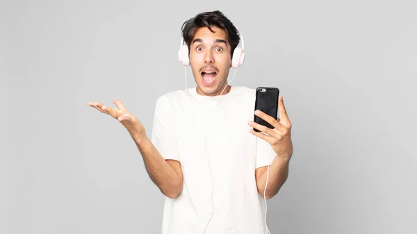 Nuori Latino Mies Tunne Onnellinen Hämmästynyt Jotain Uskomatonta Kuulokkeet Älypuhelin — kuvapankkivalokuva