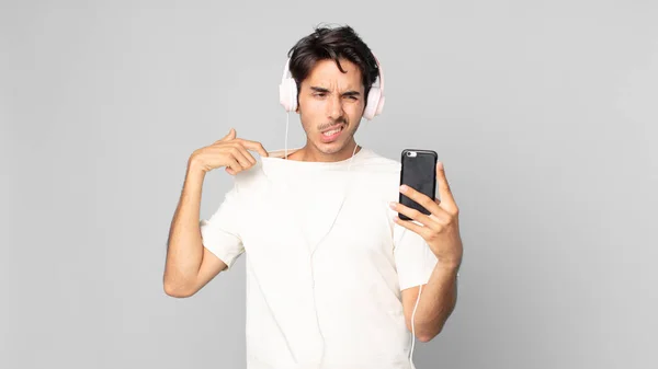 若いヒスパニック系の男性がストレスを感じ 不安を感じ ヘッドフォンやスマートフォンに不満を感じ — ストック写真