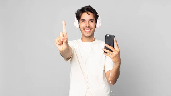 Jeune Homme Hispanique Souriant Regardant Amical Montrant Numéro Avec Écouteurs — Photo