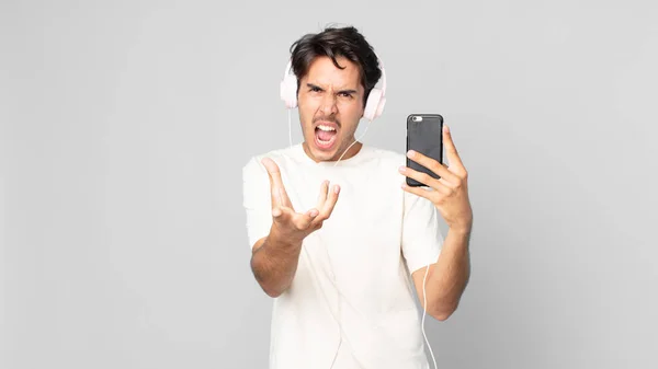 ヘッドフォンやスマートフォンに怒っていらいらしている若いヒスパニック系の男性は — ストック写真