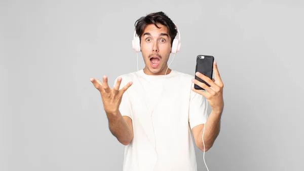 Nuori Latino Mies Tunne Erittäin Järkyttynyt Yllättynyt Kuulokkeet Älypuhelin — kuvapankkivalokuva