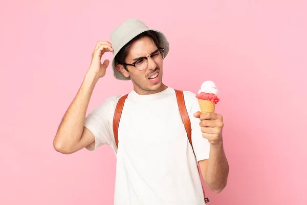若いヒスパニック系の男は困惑して混乱し頭を掻いてアイスクリームを持っています — ストック写真
