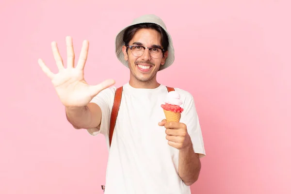 若いヒスパニック系の男は笑顔で友好的に見えます5番目を示しアイスクリームを持っています — ストック写真