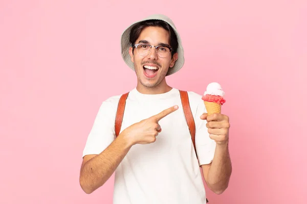 側を指差してアイスクリームを持っていることに興奮して驚いている若いヒスパニック系の男 — ストック写真