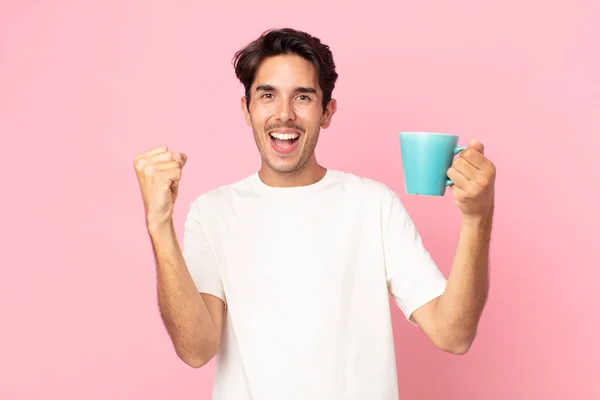 若いヒスパニック系の男性はショックを受け笑い祝い成功を収めコーヒーマグカップを持っています — ストック写真