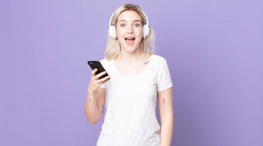 Genç ve güzel albino kadın mutlu görünüyor ve kulaklıklar ve akıllı telefonlarla hoş bir sürpriz yapıyor.