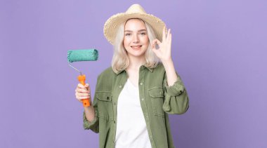 Genç, güzel, albino bir kadın kendini mutlu hissediyor. Onayını iyi bir jestle ve tekerlekli boyayla gösteriyor.