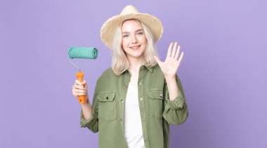 Genç ve güzel albino kadın gülümsüyor ve arkadaş canlısı görünüyor, beş numarayı gösteriyor ve tekerlekli bir boya tutuyor.