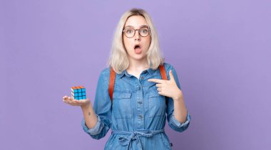 Genç, güzel, albino bir kadın ağzı açık, şok olmuş ve şaşırmış görünüyor. Kendini işaret ediyor ve bir zeka oyunu çözüyor.