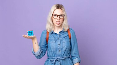 Genç, güzel, albino bir kadın. İğrenmiş ve rahatsız olmuş hissediyor. Dilini çıkarıp bir zeka oyunu oynuyor.