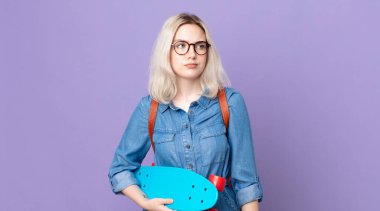 Genç, güzel albino kadın üzgün, üzgün ya da kızgın hissediyor ve elinde kaykayla yan tarafa bakıyor.