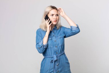 Genç, güzel albino kadın kafası karışmış ve kafası karışmış hissediyor. Kafasını kaşıyor ve akıllı telefonuyla konuşuyor.