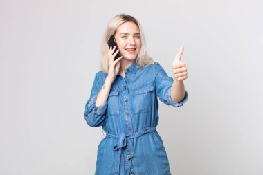 Genç, güzel albino kadın gururlu, olumlu gülümsüyor ve akıllı telefonuyla konuşuyor.