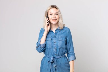 Genç ve güzel albino kadın mutlu görünüyor ve hoş bir şekilde şaşırmış ve akıllı bir telefonla konuşuyor.