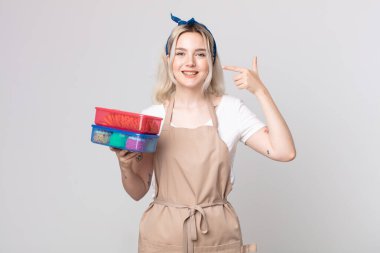 Genç, güzel, albino bir kadın, kendine güvenerek gülümsüyor. Elinde yiyecek taşıyan geniş bir gülümsemeyi işaret ediyor.