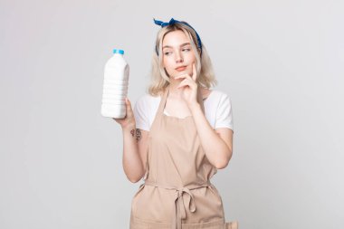 Genç ve güzel albino kadın mutlu bir şekilde gülümsüyor ve hayal kuruyor ya da bir şişe sütle şüpheye düşüyor.