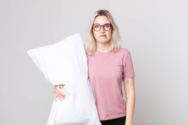 Genç, güzel albino kadın kafası karışmış görünüyor pijama giyiyor ve yastık tutuyor.