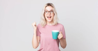 Genç, güzel albino kadın şoke olmuş, gülüyor ve kahve fincanıyla başarıyı kutluyor.