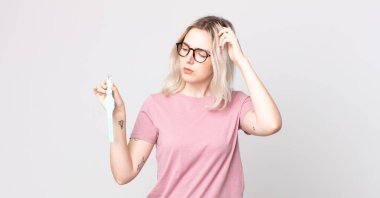 Genç, güzel albino kadın şaşkın ve kafası karışmış hissediyor. Elinde bir saat tutuyor.