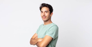 İspanyol yakışıklı adam kameraya çapraz kollarıyla gülümsüyor ve mutlu, kendinden emin, tatmin olmuş bir yüz ifadesi var.