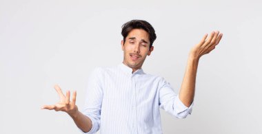 hispanic handsome man shrugging with a dumb, crazy, confused, puzzled expression, feeling annoyed and clueless