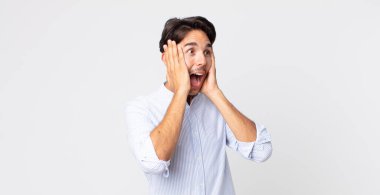 Hispanik yakışıklı adam mutlu, heyecanlı ve şaşırmış hissediyor, iki eli yüzü yana bakıyor