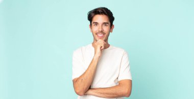 İspanyol yakışıklı adam mutlu görünüyor ve eli çenesinde gülümsüyor, merak ediyor ya da soru soruyor, seçenekleri karşılaştırıyor.